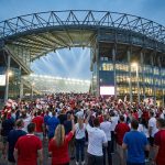 Foule de supporters en rouge et blanc marchant vers le stade de Twickenham sous une structure métallique imposante.