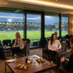 Personnes dans une loge luxueuse avec vue panoramique sur un stade de rugby lors d'un match.